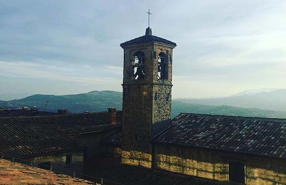 An image of a bell tower of a church with a mountainous landscape in the background during what appears to be either dawn or dusk.