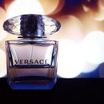 A Versace perfume bottle on a surface with a blurred background of warm lights.