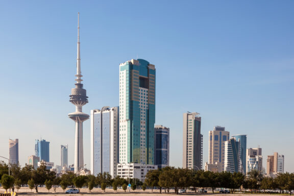 A city skyline with modern skyscrapers and a distinctive tower with a spherical structure near its top, under a clear blue sky.