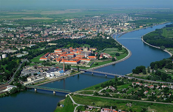 Aerial view of a city bisected by a river, with bridges and red-roofed buildings near the river bend.