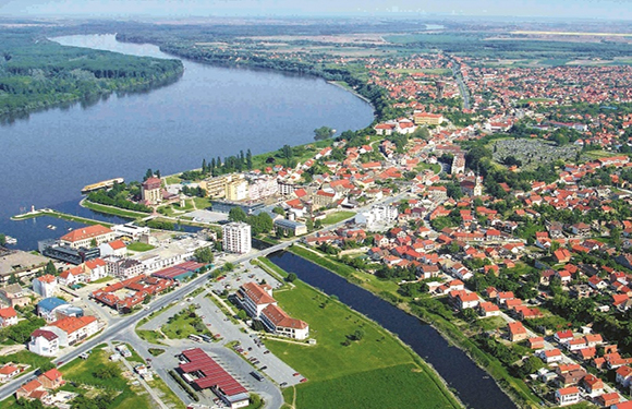 Aerial view of a town with buildings near a river, green areas, and roads.