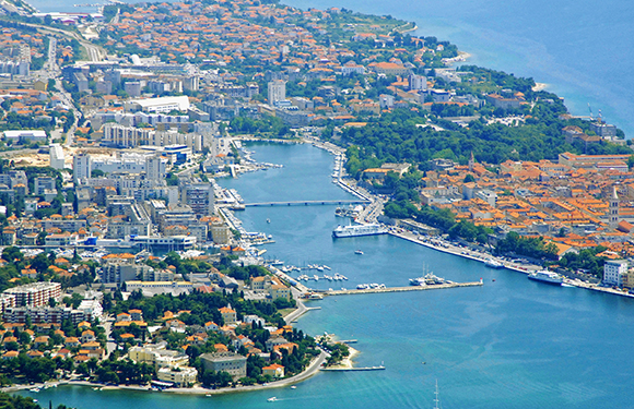 Aerial view of a coastal city with dense building clusters, a river running through the center, and bridges connecting both sides.