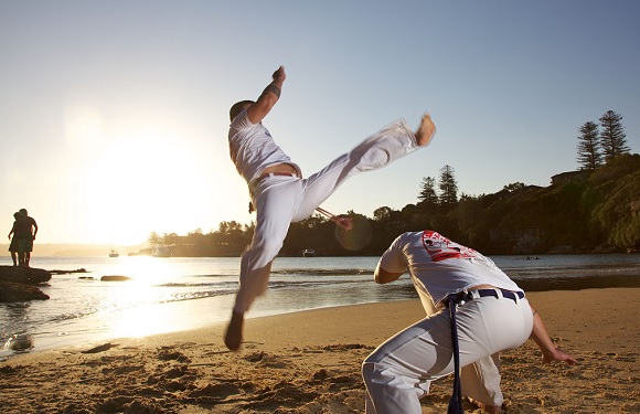 Two individuals practicing martial arts on a beach at sunset.