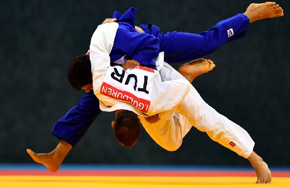 Two judo athletes, one in blue and the other in white, are competing; the blue athlete is throwing the white one on a yellow mat.