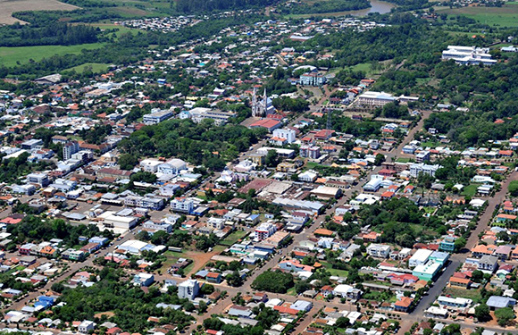 Aerial view of a small town with dense building clusters, streets laid out in a grid pattern, surrounded by greenery.