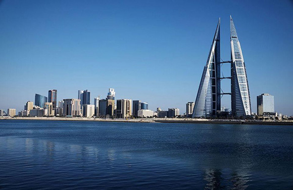 A city skyline with modern skyscrapers and a distinctive sail-shaped building near a body of water under a clear blue sky.