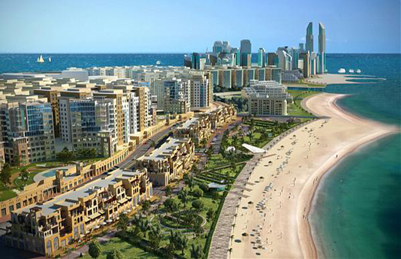 A coastal cityscape with modern high-rise buildings, a sandy beach, and a clear blue sky.