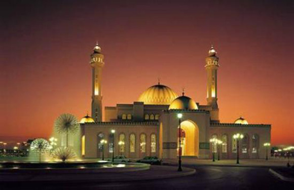 A mosque at dusk with illuminated minarets and a golden dome, against a darkening sky.