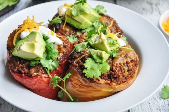 A plate with two stuffed bell peppers topped with cheese, avocado slices, and cilantro.