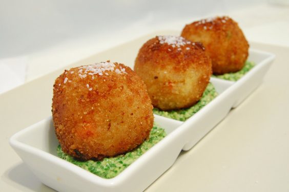 Three golden-brown, breaded balls on a white rectangular plate with a green garnish.