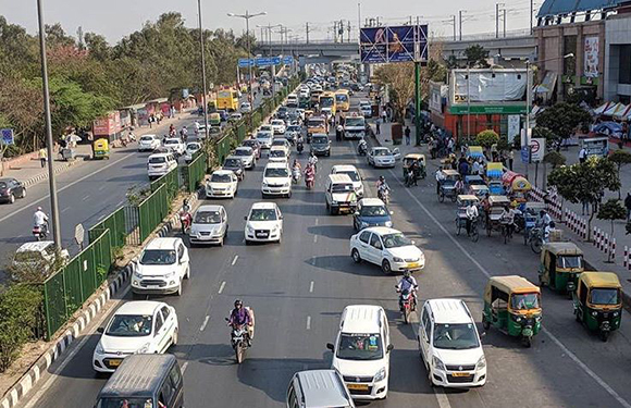 A bustling street with various vehicles, roadside billboards, and urban development on both sides.