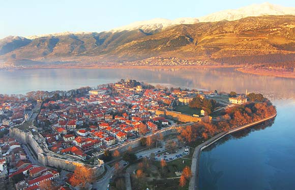 Aerial shot of a historic town on a peninsula, surrounded by a lake and mountains at sunrise/sunset.