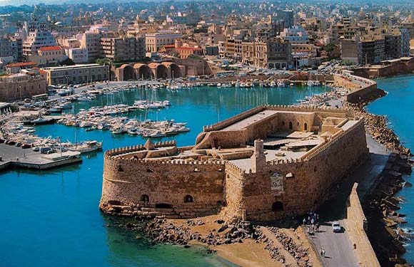 Aerial view of a coastal fortress with a marina full of boats adjacent to an urban area.