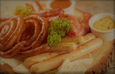 A variety of breakfast foods including bacon, sausages, and eggs on a plate with a side of sauce.