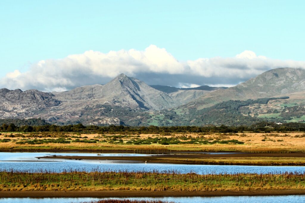 A picturesque view of Snowdonia National Park featuring mountains, a lake, grasslands, and a partly cloudy sky.