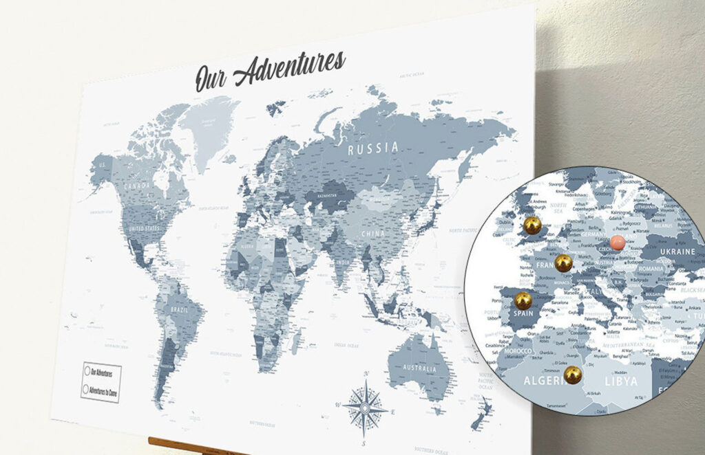 A grayscale, minimalist world map titled "Our Adventures" on a wall, marked with colored pins on visited locations.