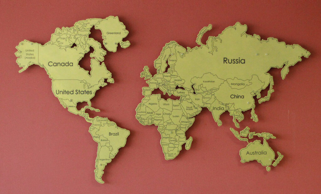 A metal wall art piece featuring a world map with country outlines and names on a red background.