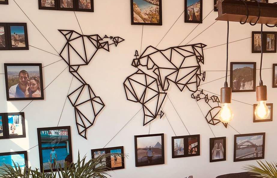 A metal world map in geometric style hanging on a wall, surrounded by various framed photographs.