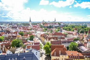 Aerial view of a historic European city with dense buildings and prominent church spires under a partly cloudy sky.