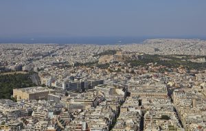 Aerial view of a crowded city, historical hill with structures in the center, under a clear sky.