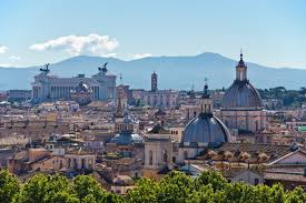 A cityscape panorama featuring historical buildings, domes, monuments, under a clear sky with distant mountains.