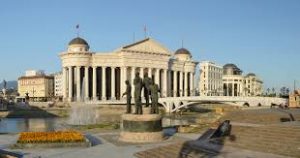 A panoramic view of a neoclassical building with columns, domes, a statue, and a fountain under a clear sky.