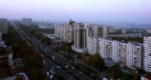 A panoramic view of a cityscape during twilight with residential buildings and a tree-lined street.