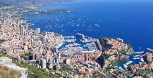 Aerial view of a coastal city with dense buildings, a port with boats, and blue sea waters.