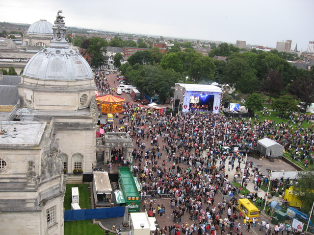 Aerial shot of a large outdoor event near a domed building, with crowds around a stage and screen.