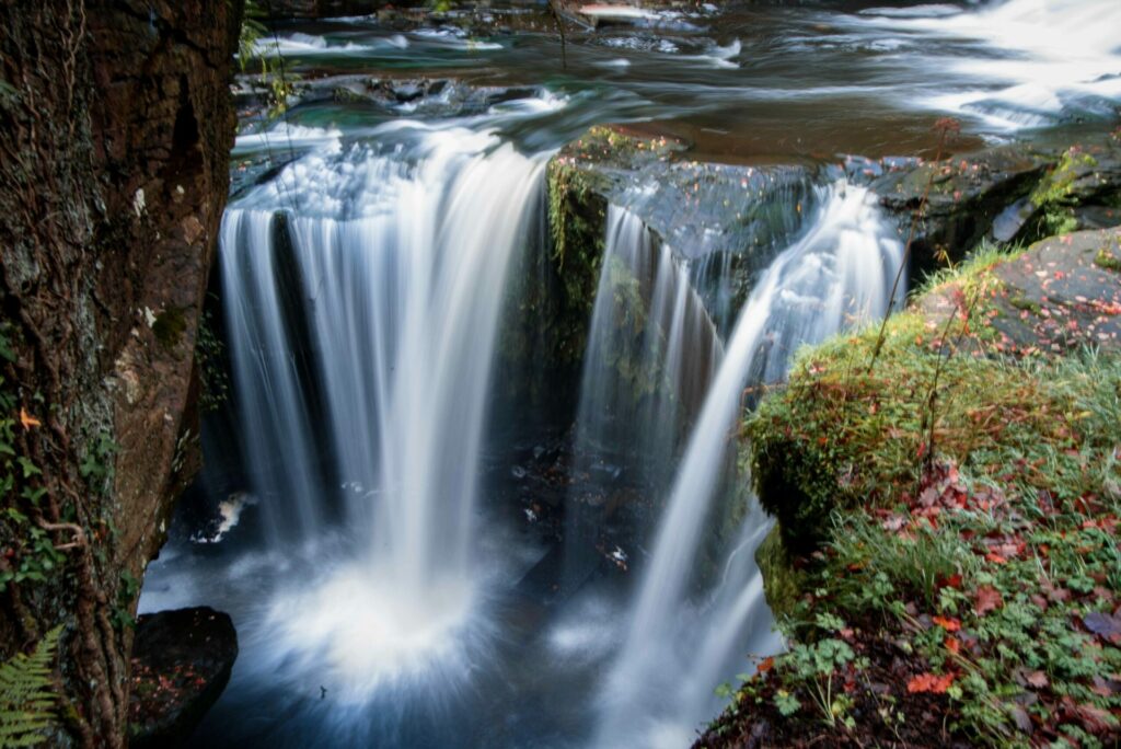 A long exposure photo of a small waterfall cascading into a pool, surrounded by rocks and greenery.