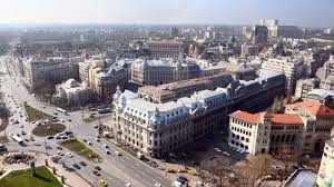 Aerial view of a city with wide streets, European-style buildings, vehicles, and scattered trees.