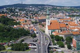 Aerial view of a city with a prominent church, roads, and buildings, with hills in the background.