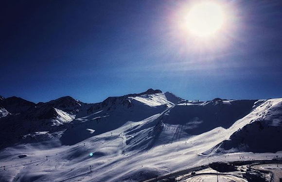 An image of a snowy mountain landscape under a bright sun with clear blue skies.