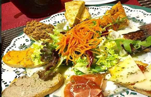 A plate with an assortment of food including slices of cheese, cured meats, salad, and bread on a tablecloth.