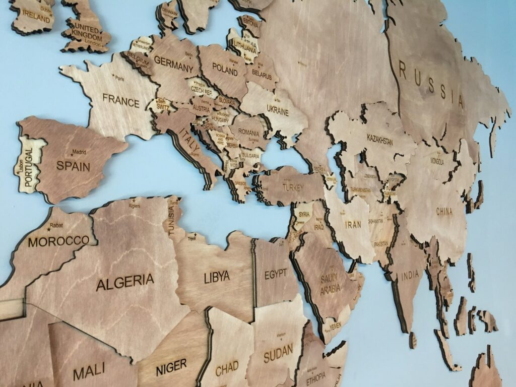 A stylized wooden world map, focusing on Europe, Africa, and parts of Asia, is mounted on a blue wall.