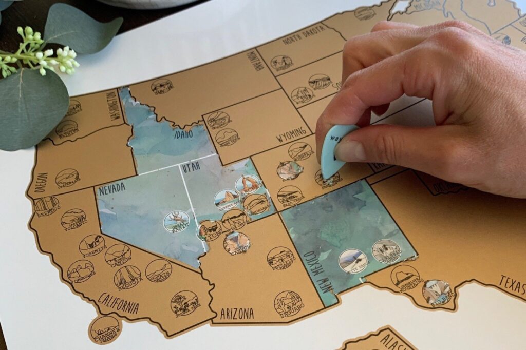 A person is revealing illustrations and info on a gold scratch-off map of US National Parks.