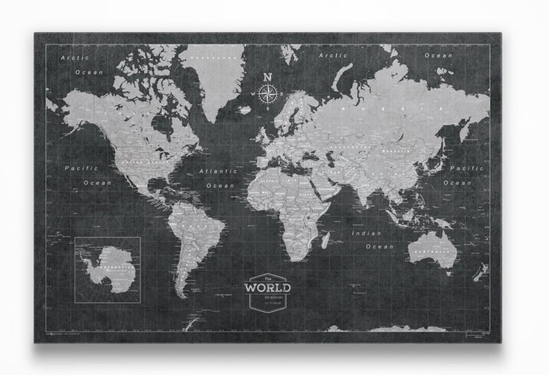 A framed world map in grayscale with push pins marking locations on a cork board background.