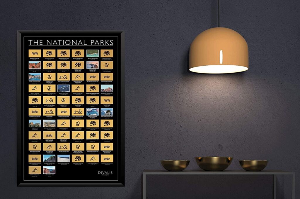 A framed USA National Parks poster is on a dark wall, lit by a lamp, with a shelf of decorative bowls below.