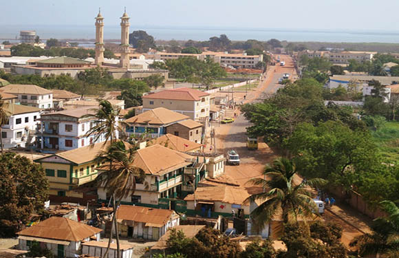 Aerial view of a street in Gambia with buildings on either side and two minarets in the distance.