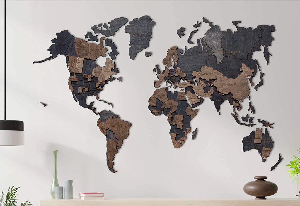 A wooden world map in various shades of brown and black mounted on a white wall, with decorative items on a surface below.