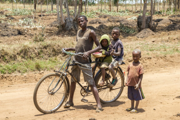 Four children with a bicycle in a rural, sparsely vegetated setting.