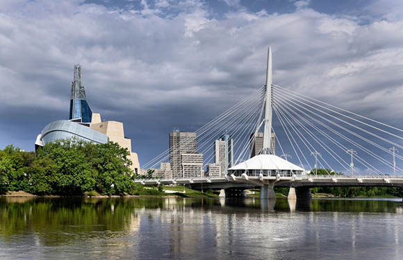 A cityscape with modern architecture, a cable-stayed bridge, a unique museum, skyscrapers, and partly cloudy skies.