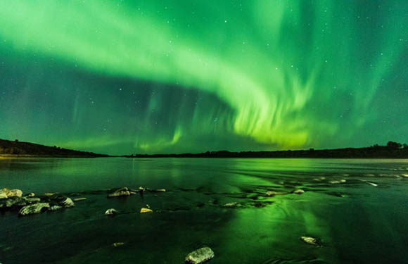 Aurora borealis (Northern Lights) over a body of water with a night sky and visible shoreline.