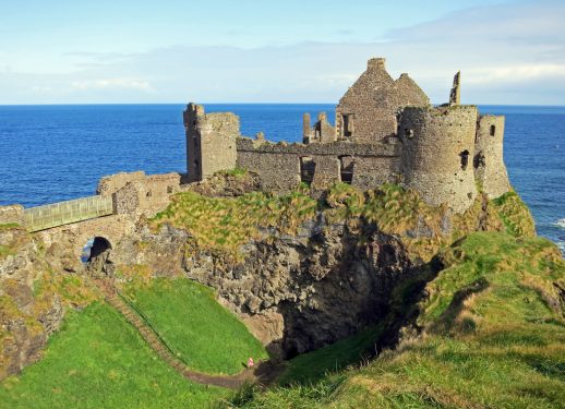 A ruined castle on a coastal cliff with the ocean in the background.