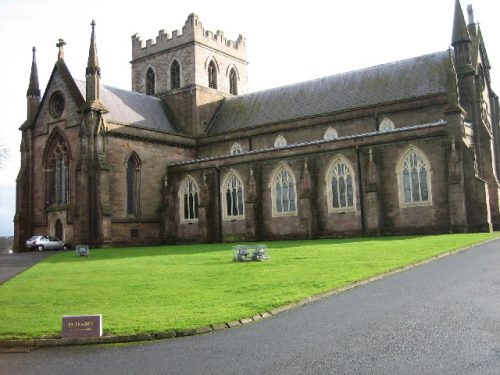 A small, traditional stone church with a pitched roof and an arched entrance, surrounded by a well-kept lawn and a clear sky in the background.