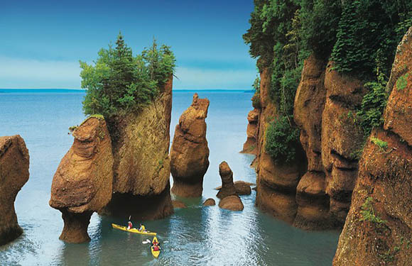 A photo of the Hopewell Rocks at low tide with a kayak navigating between the rock formations.