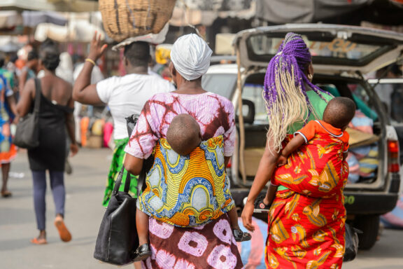 A vibrant street scene with people, including women in traditional attire, vehicles, and urban activity.