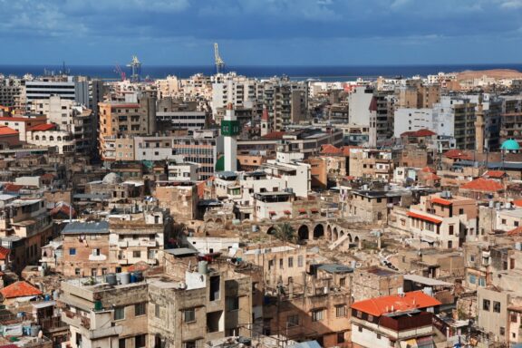 Aerial view of Tripoli, Lebanon, showcasing a dense mix of modern and traditional buildings with the Mediterranean Sea visible in the background.