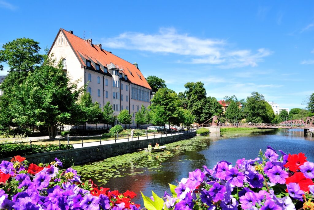 A scenic city river view with a historic building, vibrant flowers, and a clear blue sky.