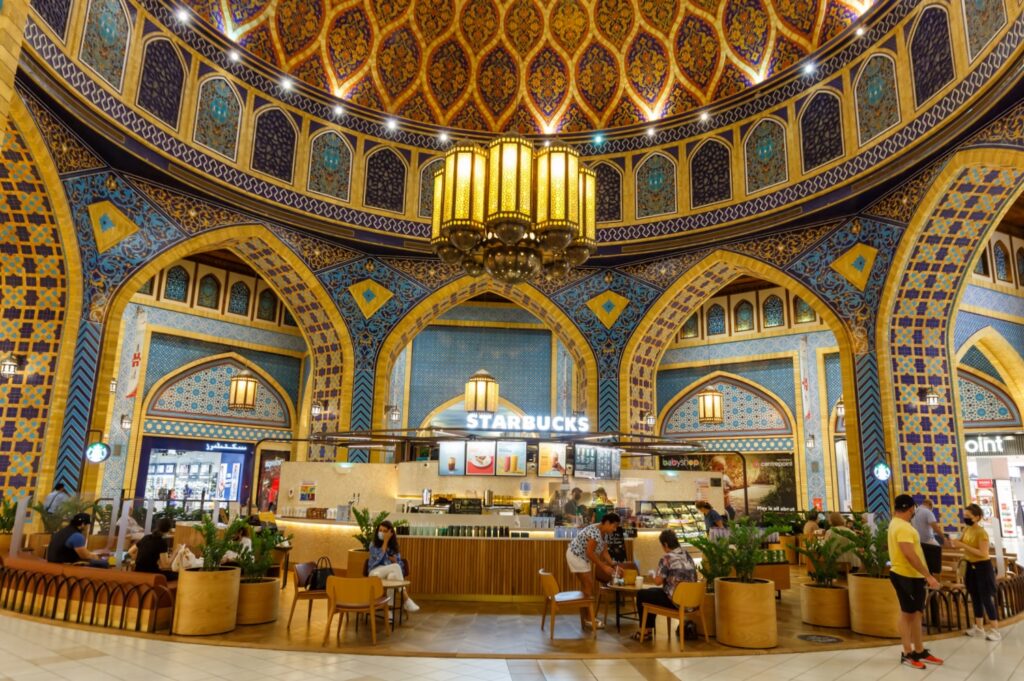 A Starbucks in a mall features Middle Eastern designs. Customers are seated around the shop.